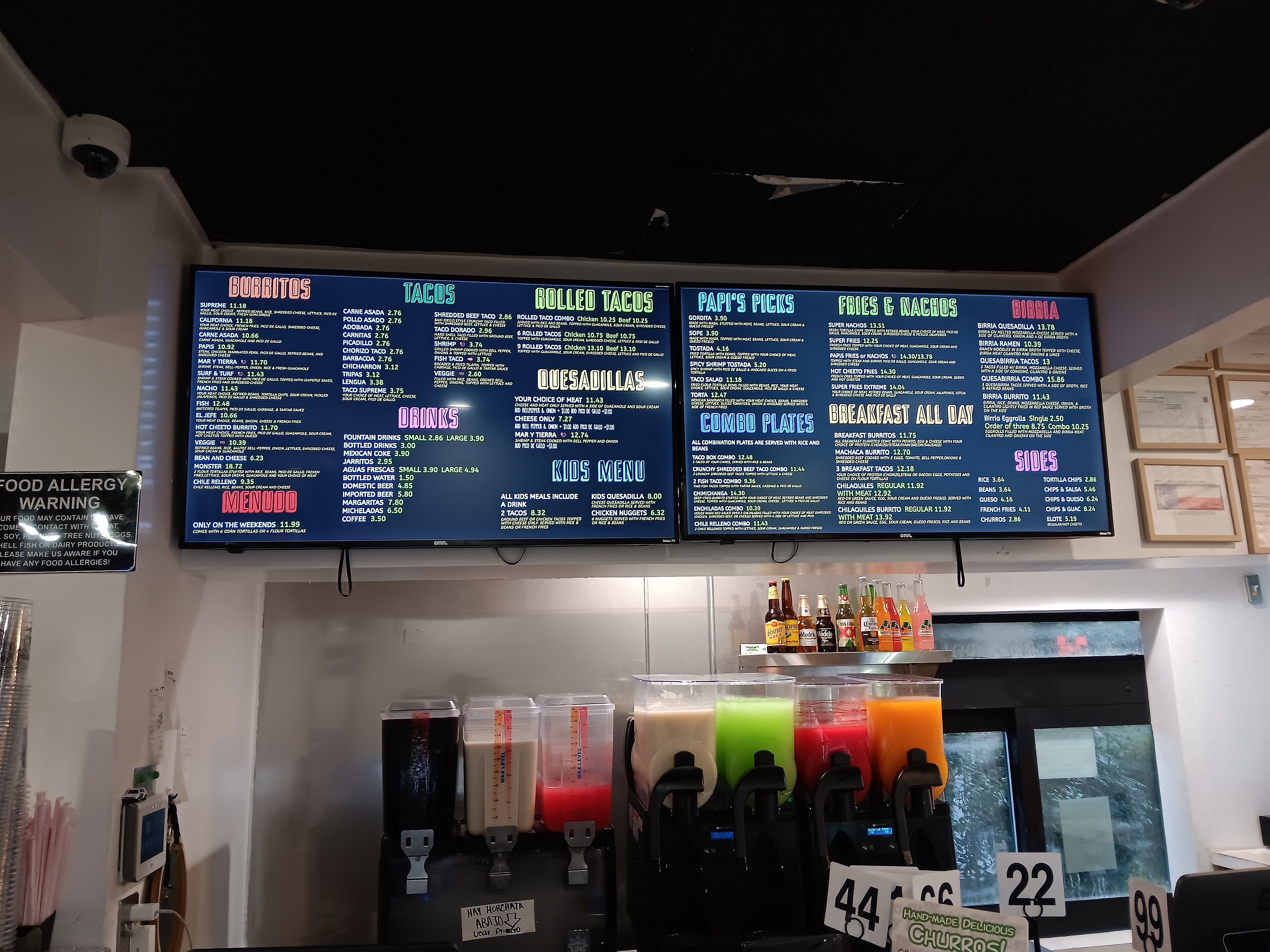 A café counter with two wide digital menu screens above the drinks machines