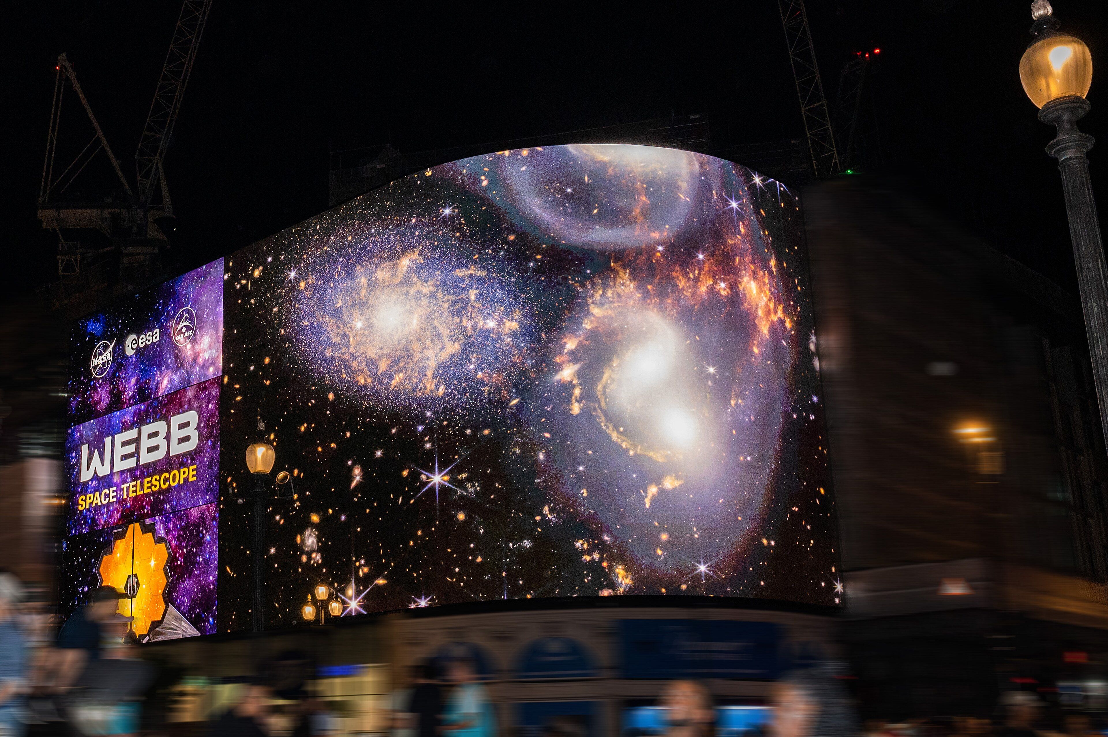 The curved Piccadilly Lights advertising screen at night showing space telescope images